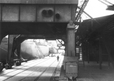 Photo mit Blick durch einen Schiffskran auf das Autoschiff MS JOHANN SCHULTE. Das Schiff wird im Emder Hafen mit VW-Käfern beladen, die in die USA exportiert werden sollen. 1967.