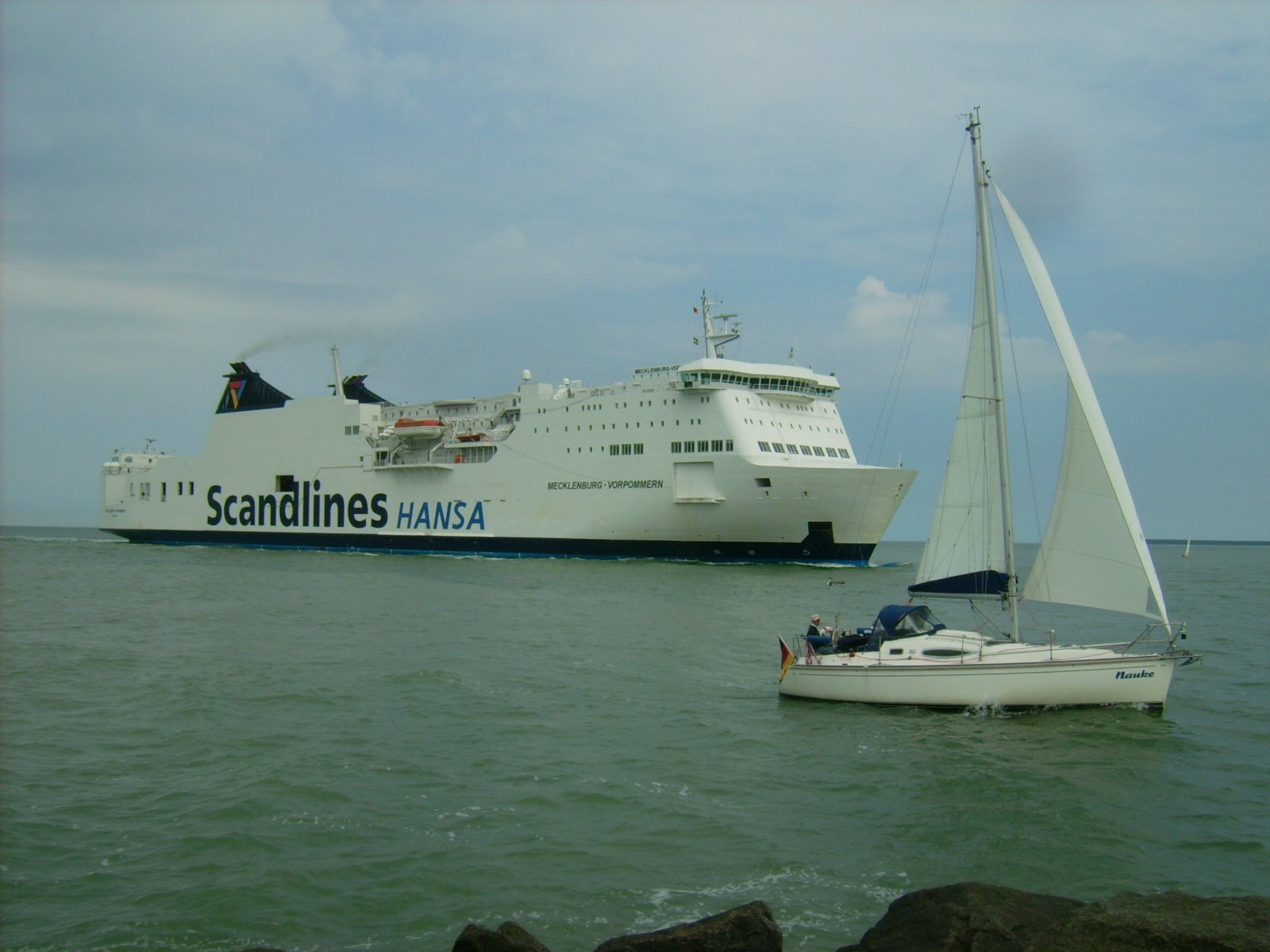 Farbphoto: Das aus Trelleborg in Schweden kommende Fährschiff FS Mecklenburg-Vorpommern im Juni 2009 bei den Anfahrt auf den Hafen von Rostock in Deutschland. Und ein Segelboot in Warnemünde. Photograph: Bernd Paepcke.